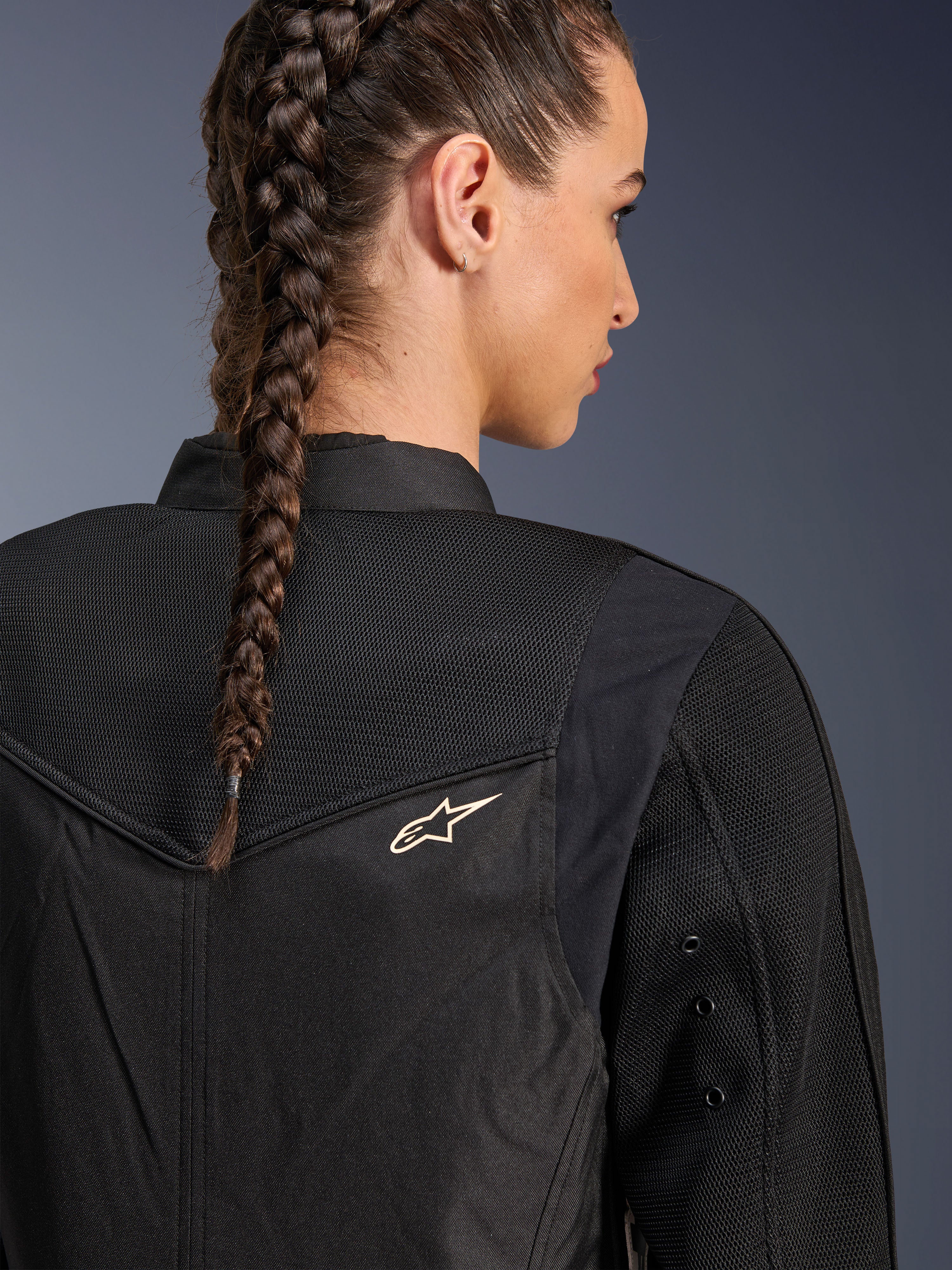 Alpinestars Stella T-Dyno Air Jacke, Damen-Motorradjacke in Schwarz, Nahaufnahme der Rückseite mit 3D-Mesh-Einsätzen an der Passe und am oberen Rücken für Luftzirkulation, kleines weißes Stern-Logo, getragen von einem Model mit geflochtenem Haar.