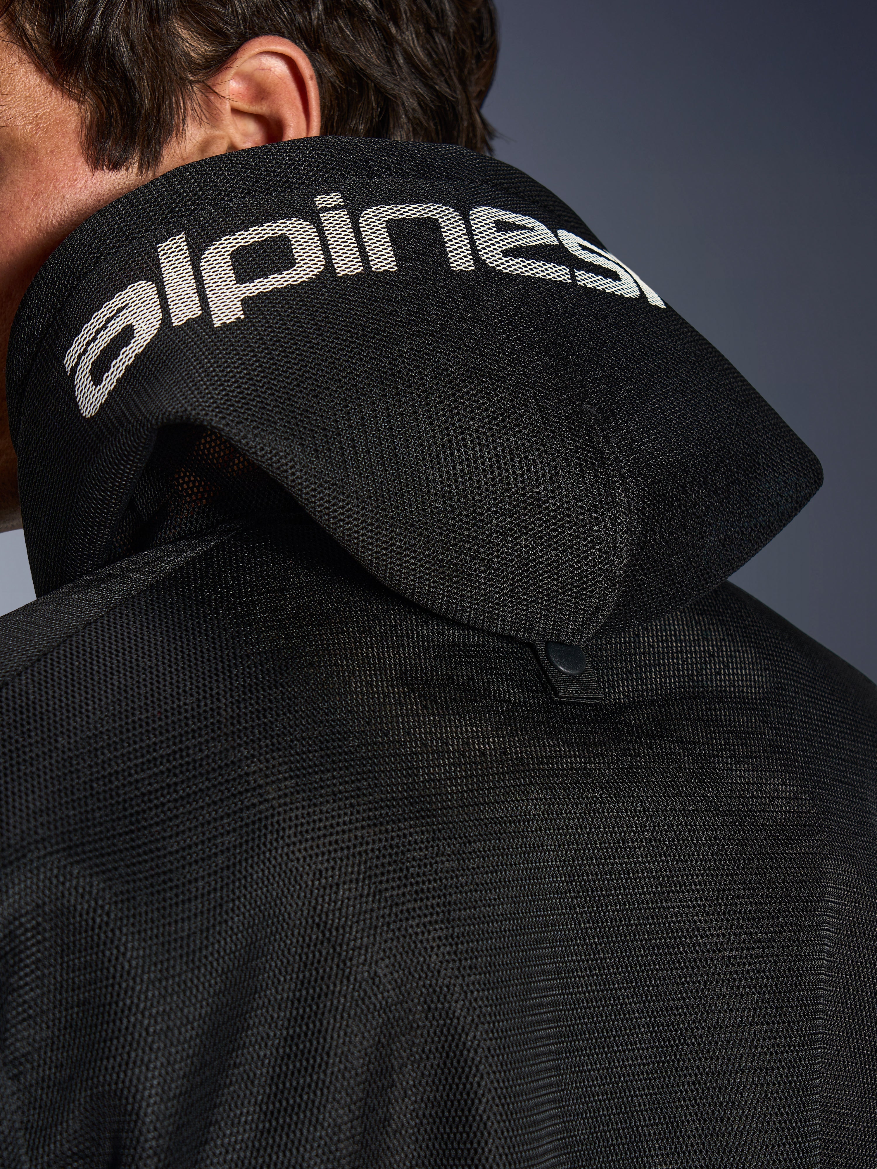 Alpinestars Chrome Superairflow Hoodie, Schwarz, Detailansicht der 3D-Mesh-Kapuze mit weißem Alpinestars-Branding auf der Oberseite, zeigt den rückseitigen Stabilisierungs-Druckknopf, belüftete Textil-Motorradausrüstung für extreme Hitze