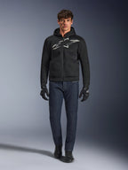 Motorradfahrer trägt den Alpinestars Chrome Superairflow Hoodie in Schwarz und Grau, kombiniert mit dunkelblauer Jeans, schwarzen Motorradhandschuhen und schwarzen Schuhen. Der Hoodie verfügt über ein großes stilisiertes Logo auf der Brust und eine 3D-Mesh-Struktur für Performance bei hohen Temperaturen.