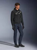 Alpinestars Chrome Superairflow Hoodie, schwarz mit weißem und grauem Logo, belüftete 3D-Mesh-Textilkonstruktion, getragen mit dunkelblauen Denim-Jeans und schwarzen Motorradhandschuhen, urbaner sportlicher Fahrstil.