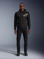 Alpinestars Chrome V2 Sport Hoodie, schwarz-weißer Motorrad-Hoodie, mit einem großen weißen Alpinestars-Logo auf der Brust, Reißverschluss vorne und Kapuze, getragen von einem Modell in schwarzer Hose und Stiefeln, urbane Motorrad-Schutzausrüstung.