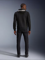 Alpinestars Chrome V2 Sport Hoodie, Motorrad-Hoodie, Schwarz, Rückansicht eines Models mit schwarzem Tech-Fleece-Hoodie und weißem Alpinestars-Logo auf der Kapuze, kombiniert mit schwarzer Hose und Stiefeln, lässiger urbaner Fahrstil