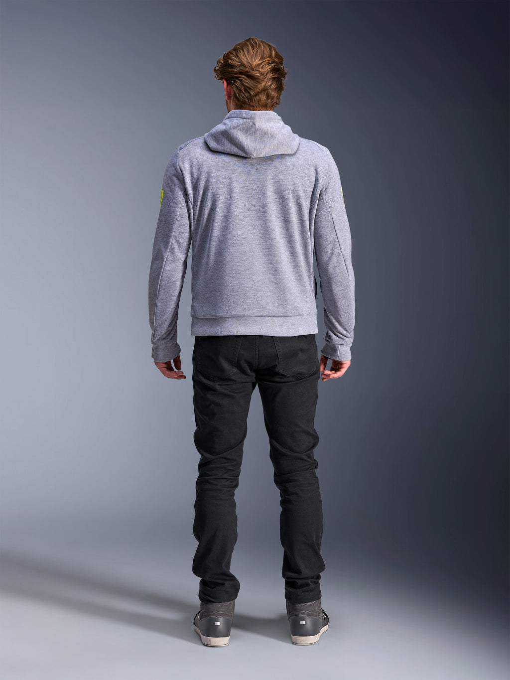 Alpinestars Chrome V2 Sport Hoodie, Grau Meliert Fluogelb, Rückansicht urbaner Motorradbekleidung, Tech-Fleece-Kapuzenpullover kombiniert mit einer schwarzen Hose, mit fluorgelben Akzenten an den Ärmeln