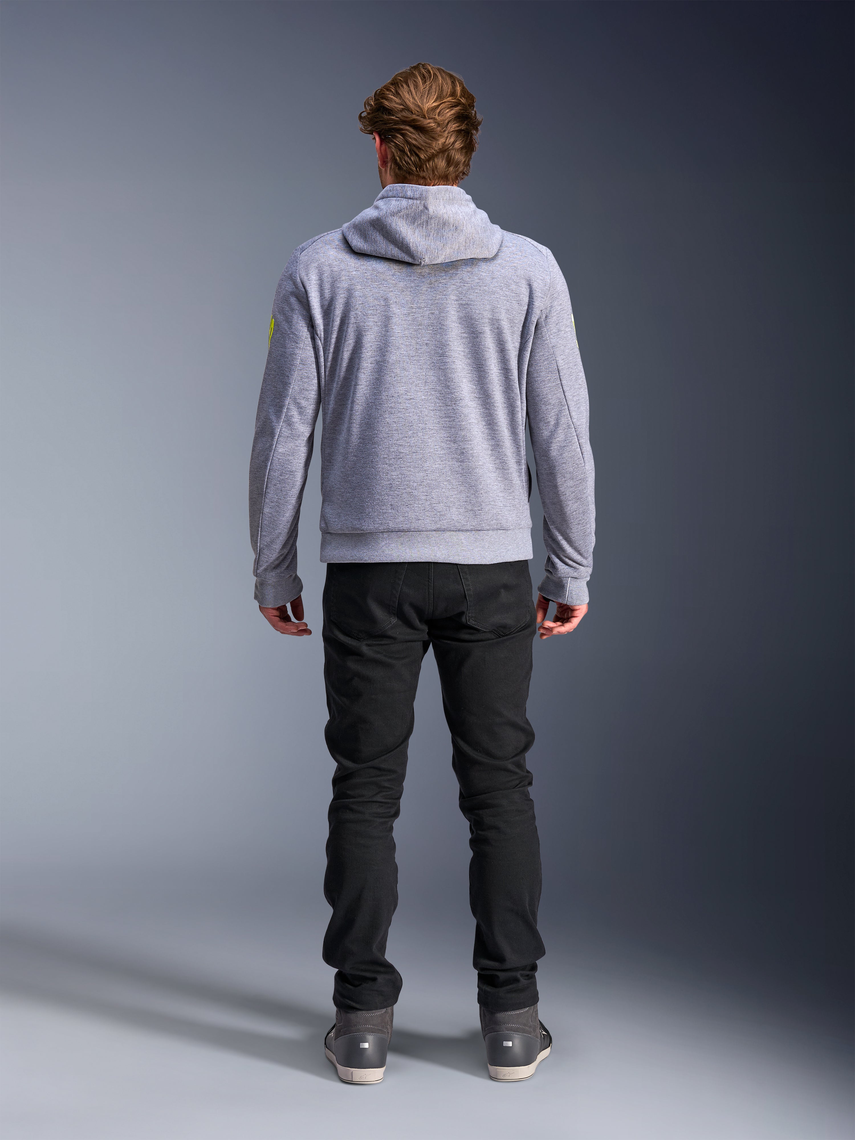 Alpinestars Chrome V2 Sport Hoodie, Grau Meliert Fluogelb, Rückansicht urbaner Motorradbekleidung, Tech-Fleece-Kapuzenpullover kombiniert mit einer schwarzen Hose, mit fluorgelben Akzenten an den Ärmeln