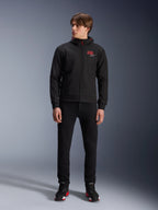 Alpinestars MM93 Radium Tech Hoodie, black urban motorcycle hoodie, featuring a red 93 logo and white star logo on the chest, worn by a model with black pants and matching riding shoes, sleek windproof technical shell for urban riding.
