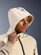 Alpinestars Radium Tech Hoodie in Mastic Aluminum, close-up of a man wearing the hood up, featuring Alpinestars branding on the top, urban motorcycle jacket with technical windproof shell, modern streetwear aesthetic for city riding