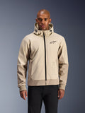 Alpinestars Radium Tech Hoodie in Mastic Aluminum, light beige and tan urban motorcycle jacket, black front zipper and small chest logo, modeled by a man in black pants, technical windproof shell with contemporary streetwear styling