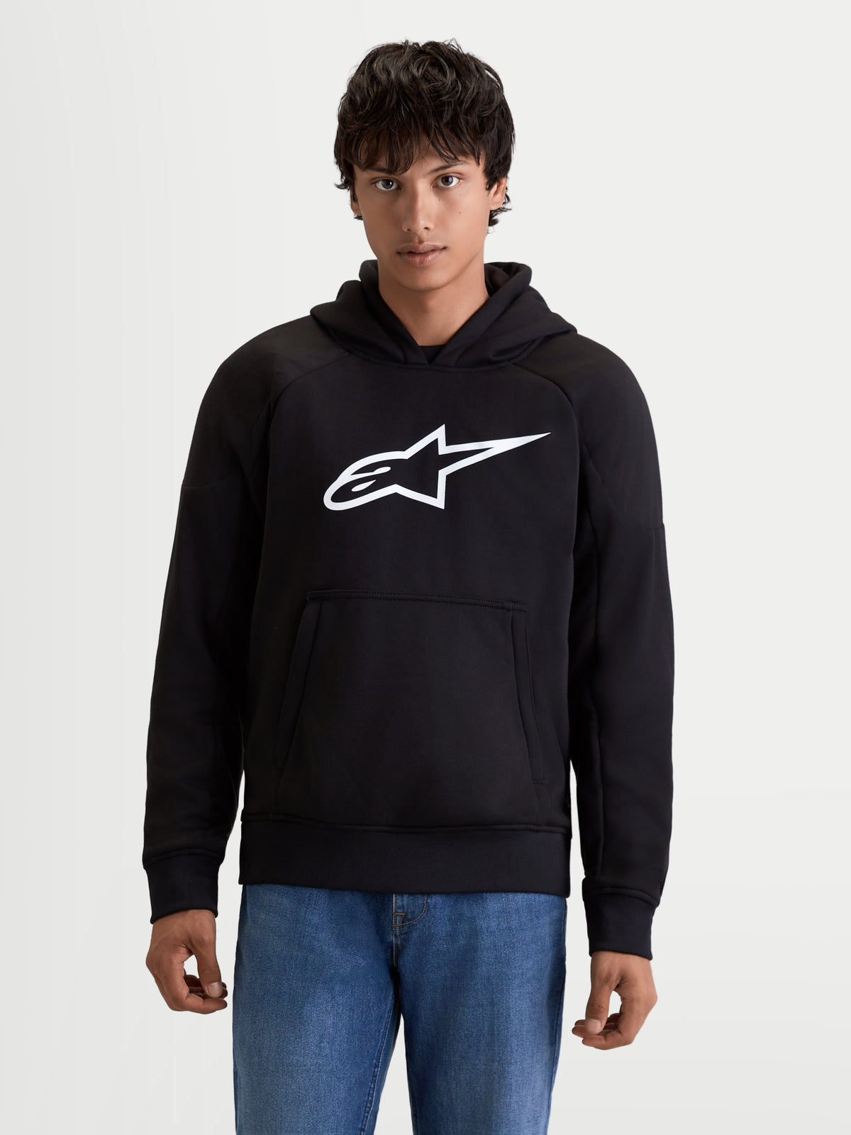 Alpinestars Ageless Kapuzenpullover, urbaner Herren-Motorradhoodie in Schwarz mit weißem Logo auf der Brust, Kängurutasche auf der Vorderseite und lässiger Textilkonstruktion, Vorderansicht an einem Model