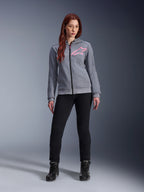 Alpinestars Stella Chrome V2 Sport Hoodie, Gray Heather Pink Fluo, getragen von einer Frau mit schwarzer Hose und Stiefeln, mit einem pinkfarbenen Alpinestars Stern-Logo auf der Brust, Urban-Motorradbekleidung mit durchgehendem Reißverschluss, leichtes Tech-Fleece mit lässiger, sportlicher Passform.