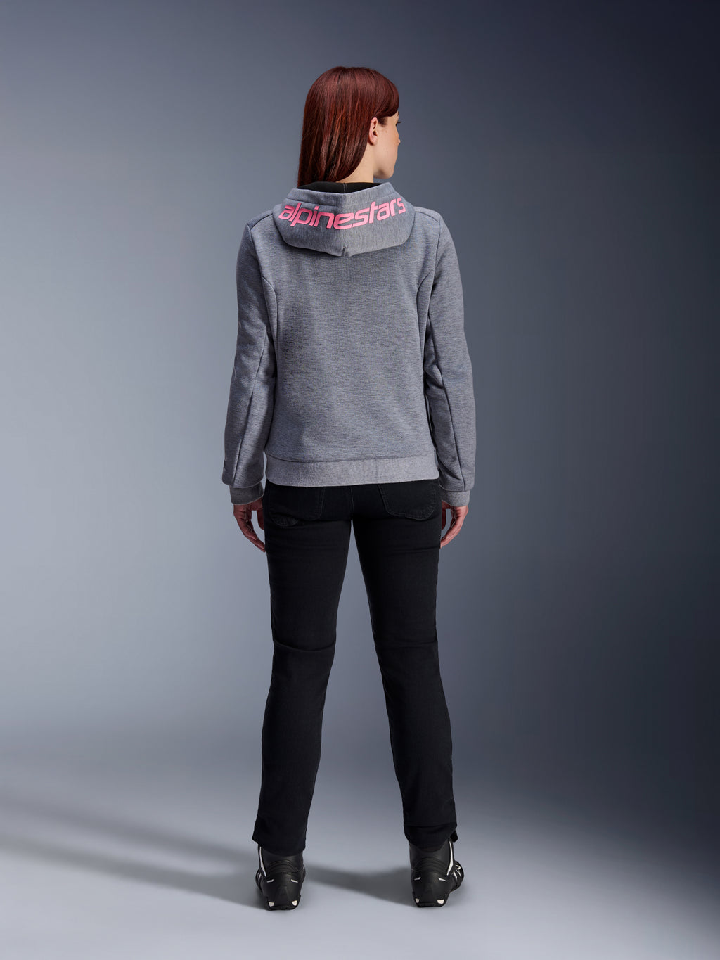 Alpinestars Stella Chrome V2 Sport Hoodie, Motorrad-Kapuzenjacke für Damen, Grau Meliert und Pink Fluo, Rückansicht mit pinkem Alpinestars-Logo auf der Kapuze, getragen mit schwarzer Motorradhose und Stiefeln, lässige Motorradbekleidung für Damen
