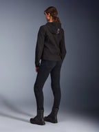 Alpinestars Stella Radium Tech Hoodie, schwarzer Urban-Riding-Hoodie für Damen, Rückansicht mit „ALPIN“-Branding auf der Kapuze, kombiniert mit schwarzer technischer Motorradhose und schwarzen Stiefeln, leichte winddichte Tech-Shell.