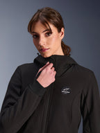 Alpinestars Stella Radium Tech Hoodie für Damen, Schwarz, getragen von einer Frau beim Einstellen des Frontreißverschlusses, mit rundem Alpinestars-Logo-Patch auf der Brust, gerippten Stretch-Bündchen und winddichter Textilkonstruktion für urbane Fahrten