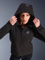 Frau trägt den Alpinestars Stella Radium Tech Hoodie in Schwarz, urbaner Motorrad-Hoodie mit aufgesetzter Kapuze, kreisförmiges Alpinestars-Logo auf der Brust, gerippte Bündchen und winddichte 3-Lagen-Konstruktion