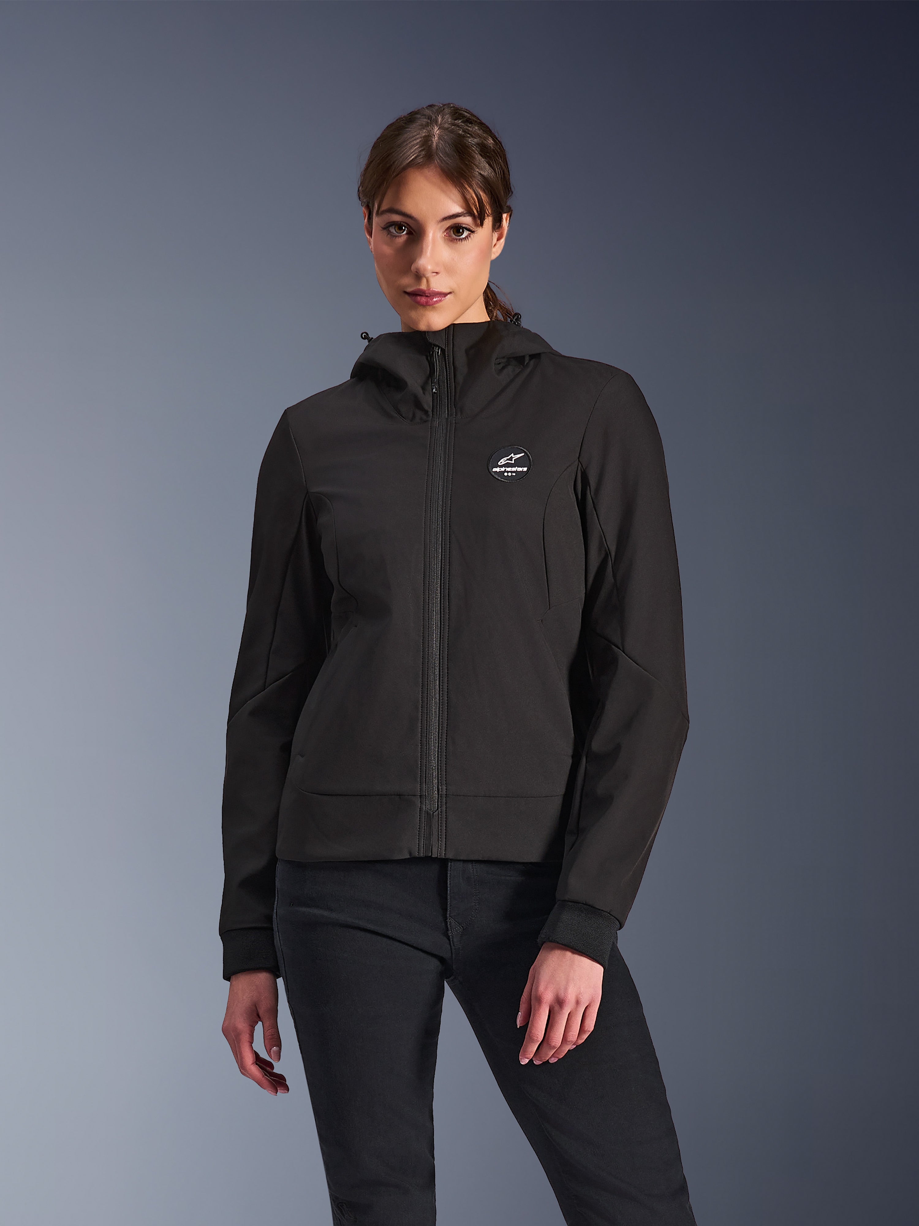 Alpinestars Stella Radium Tech Hoodie, Damen-Motorrad-Kapuzenjacke, Schwarz, Reißverschluss-Design mit rundem Brustlogo und Kapuze, technische urbane Fahrerausrüstung, von einem Model getragen