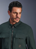 Alpinestars Bryon Water Resistant Overshirt in Dark Emerald, close-up portrait of a man wearing the urban motorcycle jacket, featuring waxed canvas texture, front zipper with subtle teal accents, chest cargo pockets, and branded logo patch.