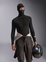 Male model wearing the Alpinestars ZX Evo V3 Balaclava in Black, featuring white logos on the forehead and chin, paired with a black long-sleeve base layer top and holding a carbon fiber racing helmet, professional flame-resistant motorsport gear for auto racing.