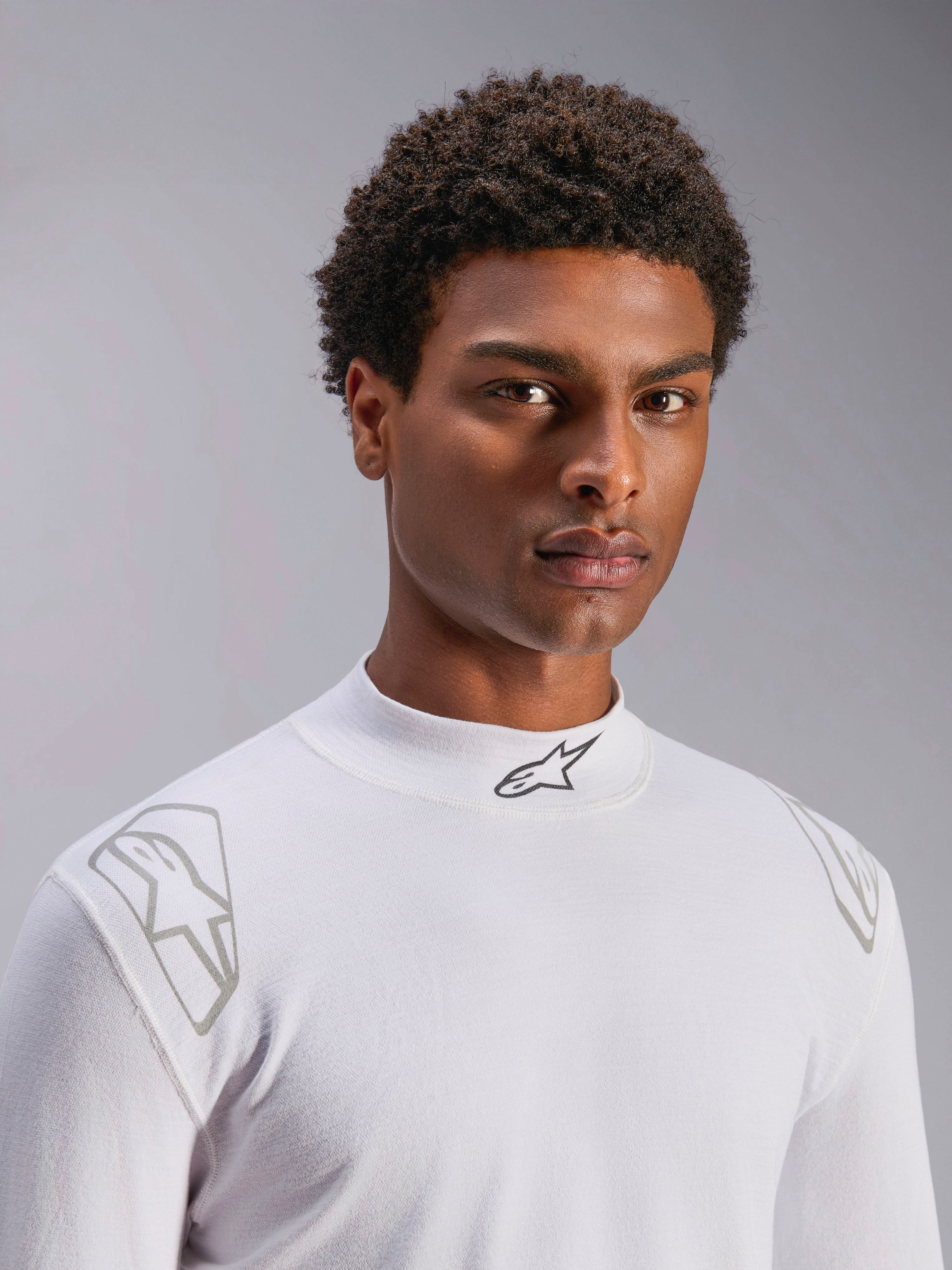 Alpinestars ZX Evo V3 Langarm-Oberteil, weißer Auto-Rennsport Base Layer, von einem männlichen Model getragen, Stehkragen mit schwarzem Alpinestars-Logo, silberne Grafikdrucke auf den Schultern, leichte flammhemmende Motorsport-Unterwäsche