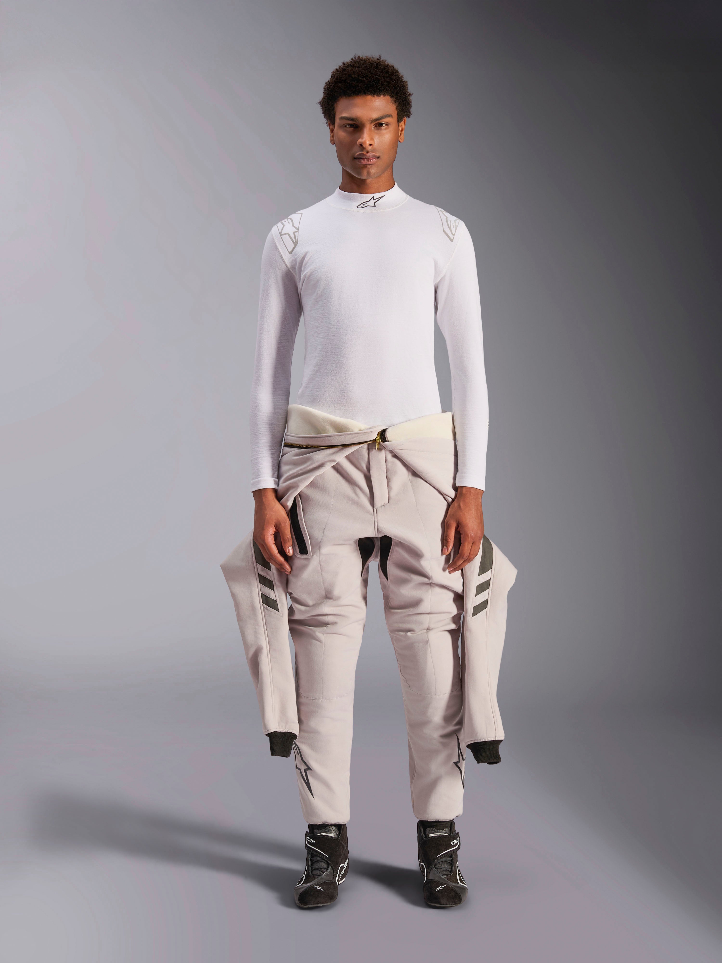 Alpinestars ZX Evo V3 Top, Langarm, Weiß, Auto-Rennsport-Basisschicht, getragen mit einem hellen Rennanzug um die Taille und schwarzen Rennstiefeln, mit Stehkragen mit Logo und Schulter-Branding, professionelle flammenresistente Motorsport-Unterwäsche