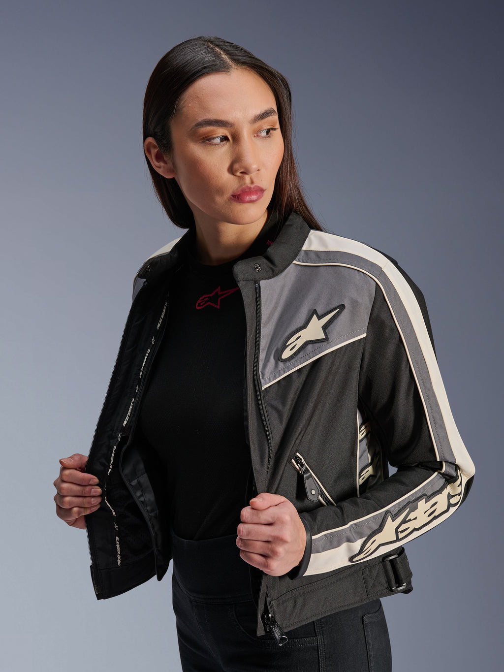 Alpinestars Stella T-Dyno WR Damenjacke, Textil-Motorradjacke, Schwarz, Dunkelgrau und Ecru, vintage-inspiriertes Design mit sportlichen Streifen und Logos auf Brust und Ärmeln, getragen von einem Model, urbane Motorradbekleidung
