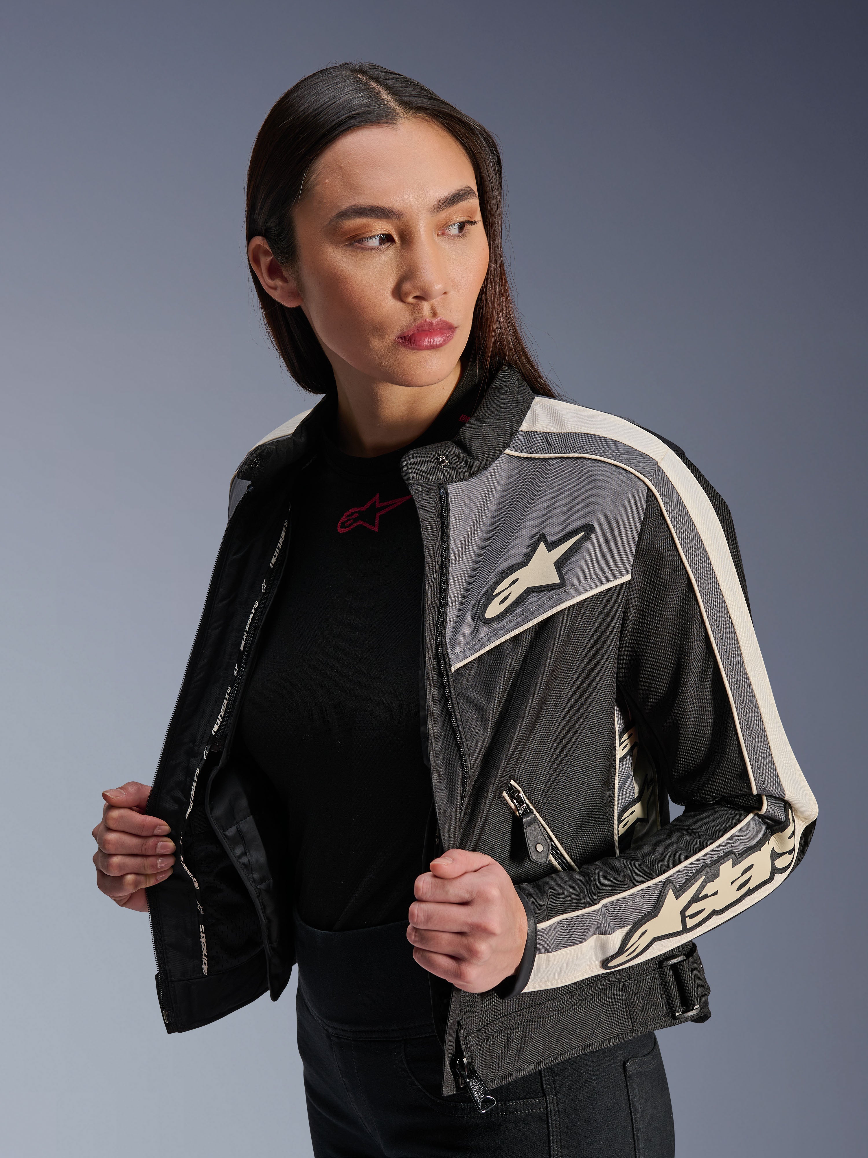 Alpinestars Stella T-Dyno WR Damenjacke, Textil-Motorradjacke, Schwarz, Dunkelgrau und Ecru, vintage-inspiriertes Design mit sportlichen Streifen und Logos auf Brust und Ärmeln, getragen von einem Model, urbane Motorradbekleidung