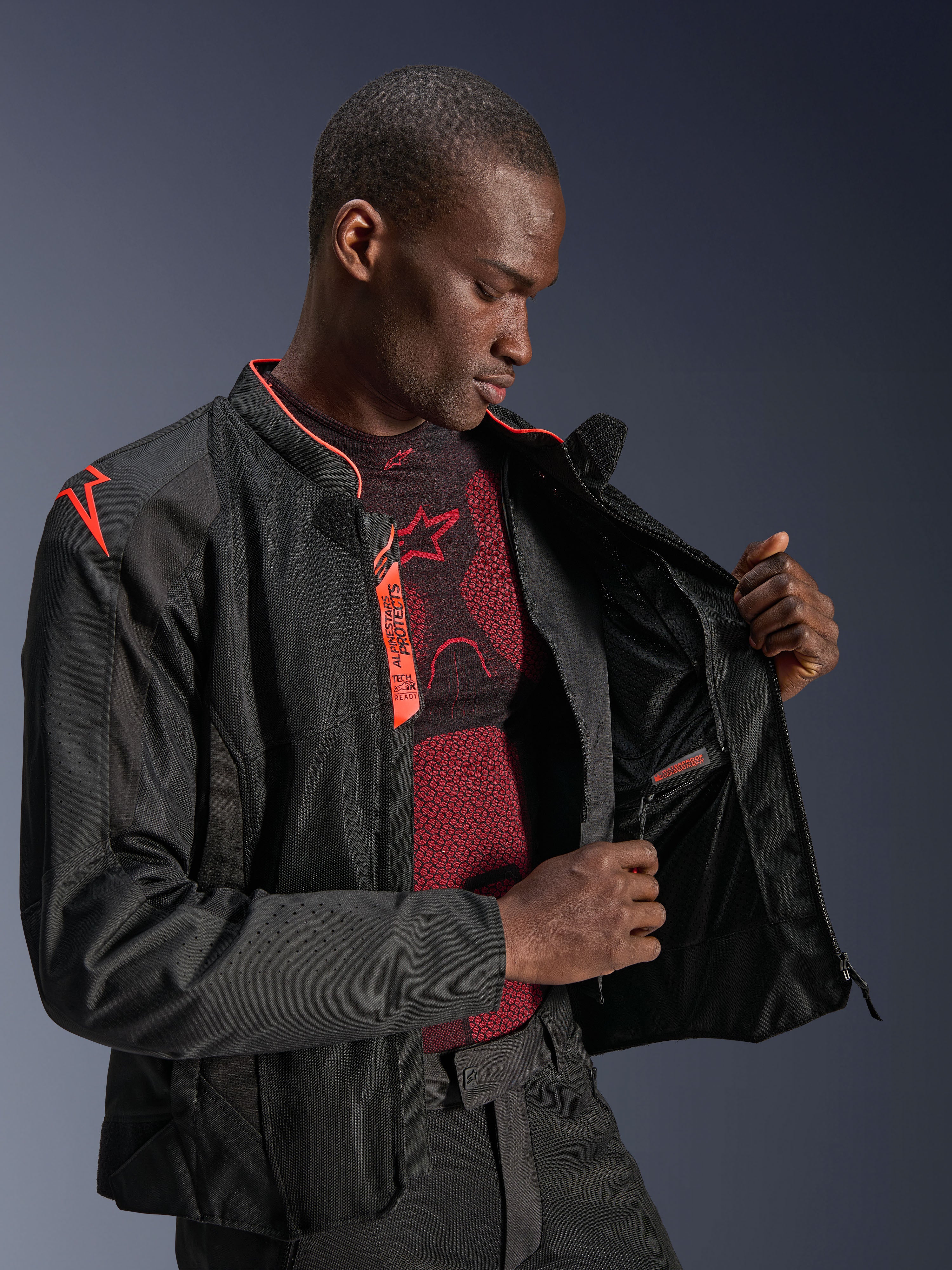 Alpinestars Viper Air V4 Jacke, Schwarz Rot Fluo, Motorradjacke mit Tech-Mesh-Einsätzen, männliches Model zeigt das wasserdichte Innenfach und das Innenfutter, mit Akzenten in fluoreszierendem Rot und Tech-Air® Ready-Branding.
