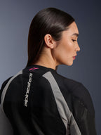 Nahaufnahme einer Frau im Profil, Alpinestars Stella Troop-Air Jacke, Mesh-Konstruktion in Schwarz und Ash Gray, vertikales weißes Alpinestars-Logo am oberen Rücken mit Stern-Logo in Pink Fluo, leichte technische Motorradbekleidung für Damen