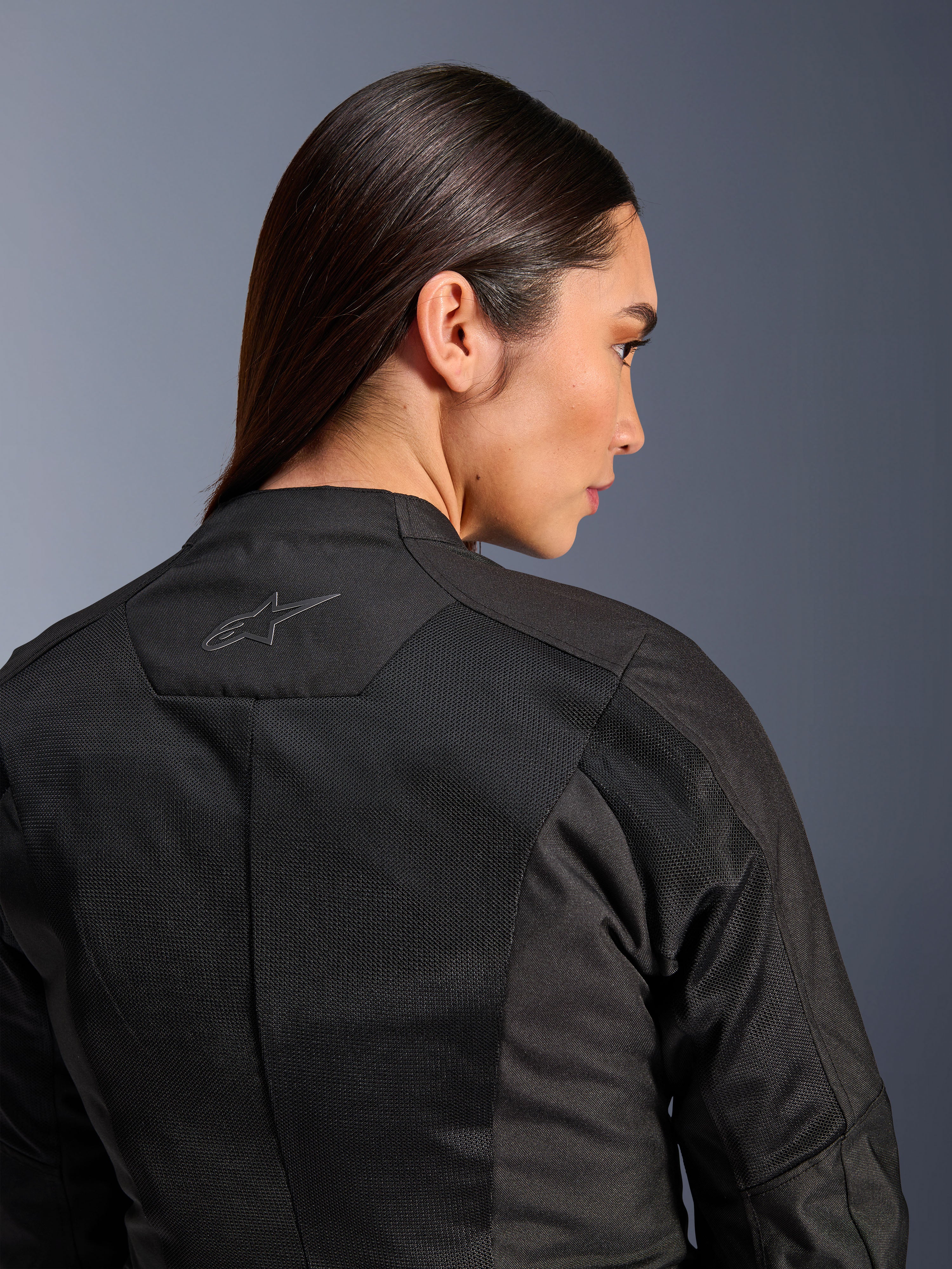 Alpinestars Stella C-1 Air Damenjacke, Textil-Motorradjacke, Schwarz, Nahaufnahme der Rückansicht mit Tech-Mesh-Belüftungseinsätzen und einem reflektierenden Stern-Logo am oberen Rücken, moderne urbane Fahrausrüstung