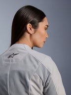 Frau in der Alpinestars Stella C-1 Air Jacke in Silber, Nahaufnahme der Seiten-Rückansicht, schwarzes Alpinestars-Logo, Tech-Mesh-Belüftungseinsätze, klares, zeitgemäßes urbanes Motorrad-Design