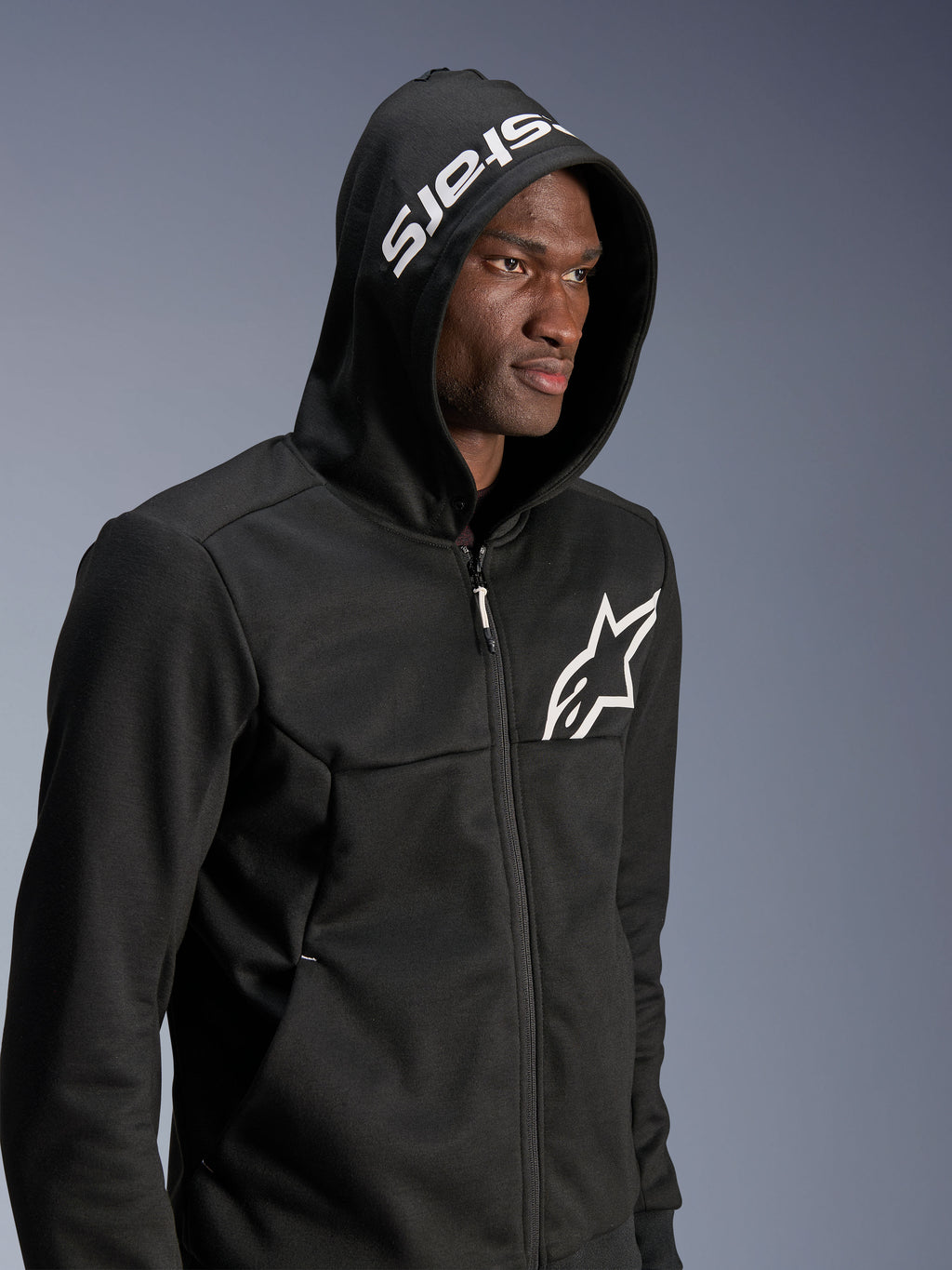 Alpinestars Chrome V2 Sport Hoodie, Schwarz, urbaner Riding-Hoodie, Model mit aufgesetzter Kapuze, weißes Sternenlogo auf der Brust und weißes „stars“-Branding auf der Kapuze, Tech-Fleece-Konstruktion, lässige Motorrad-Streetwear