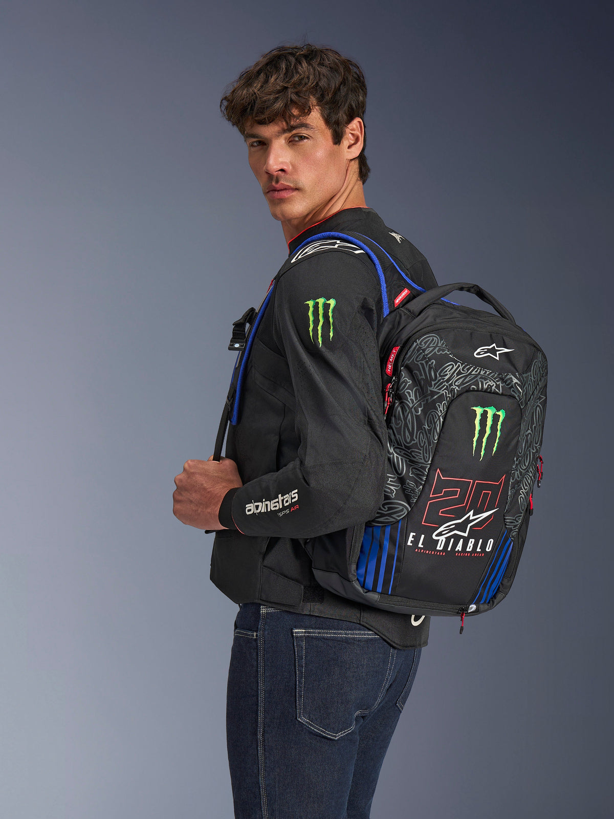 Alpinestars FQ20 City Hunter V2 Monster Rucksack, Motorradrucksack, Schwarz mit Rot Fluo, Blau und Grün, mit Monster Energy- und Fabio Quartararo 'El Diablo'-Branding, getragen von einem Model mit schwarzer Motorradjacke und Jeans, schlankes Design für urbane Fahrer