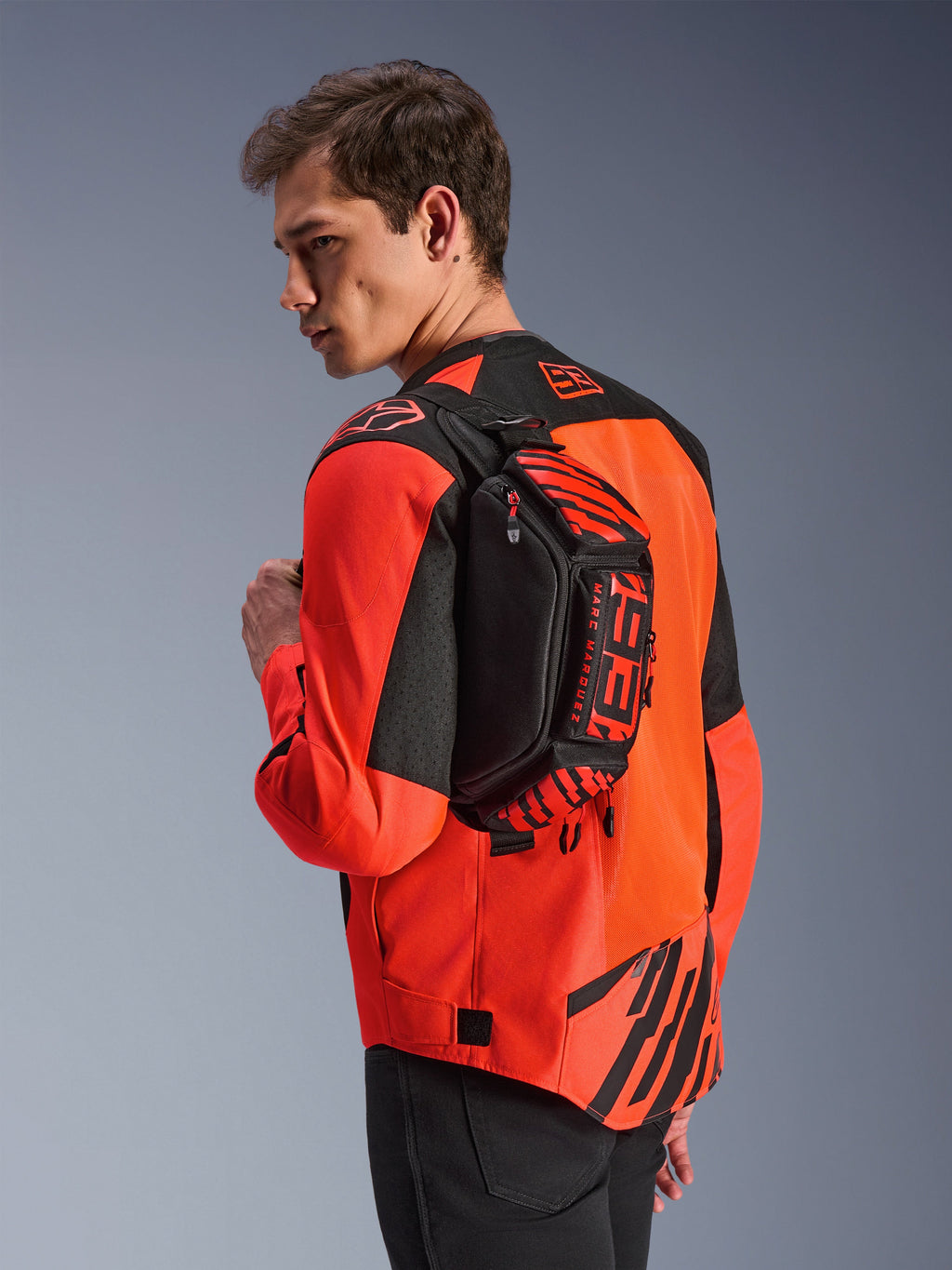Alpinestars MM93 Hüfttasche, Schwarz mit Red Fluo und Bright Red, von einem Model über dem Rücken über einer rot-schwarzen Motorradjacke getragen, mit markantem MM93-Branding und Marc-Marquez-Grafiken