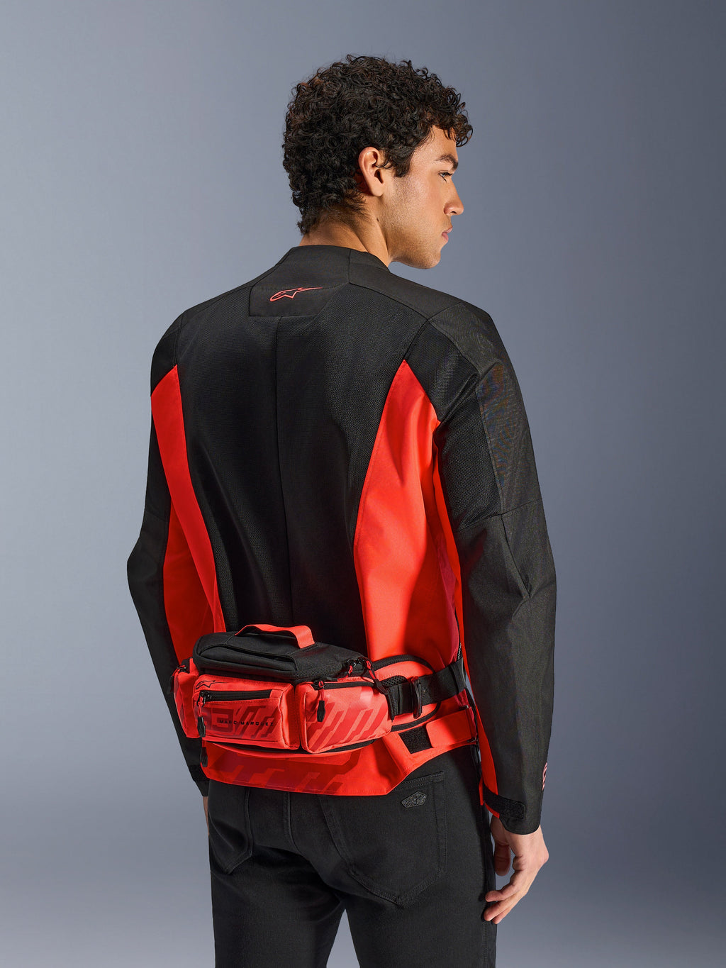 Alpinestars MM93 Hüfttasche, Motorrad-Gürteltasche, Hellrot und Schwarz, getragen über einer passenden schwarz-roten Motorradjacke, mit Reißverschlussfächern und Marc Marquez MM93-Branding, strapazierfähige Textilkonstruktion für den Motorradsport