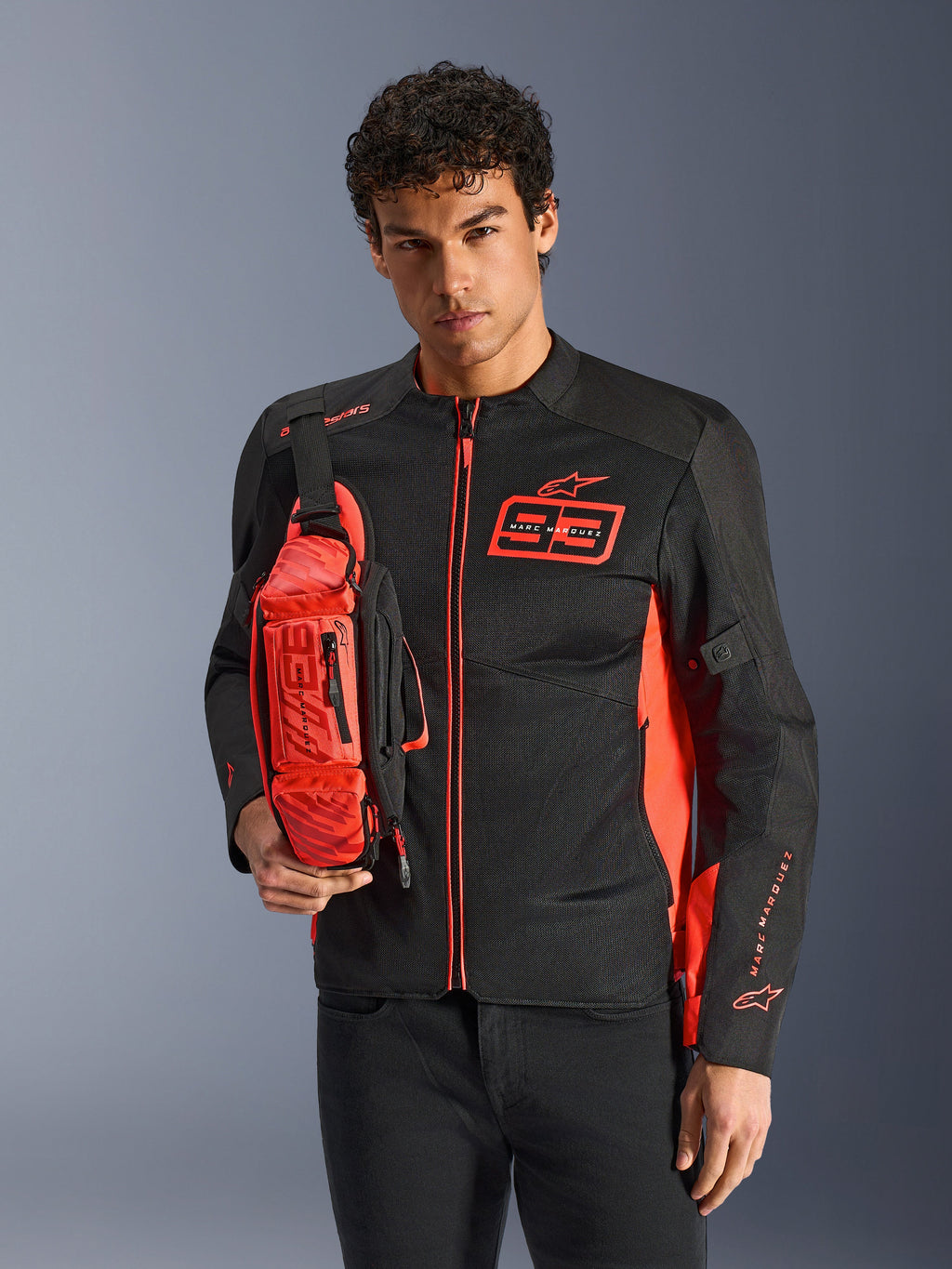Mann mit Alpinestars MM93 Waist Bag, Rot Fluo und Schwarz, als Crossbody-Tasche über einer passenden schwarz-roten Motorradjacke getragen, mit Marc Marquez 93-Logo, sportliches Racing-Design