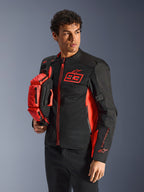 Alpinestars MM93 Hüfttasche, Red Fluo und Schwarz, gehalten von einem Model in einer passenden schwarz-roten Motorradjacke, mit mehreren Reißverschlussfächern und Marc Marquez Branding, praktische Ausrüstung für sportliches Fahren