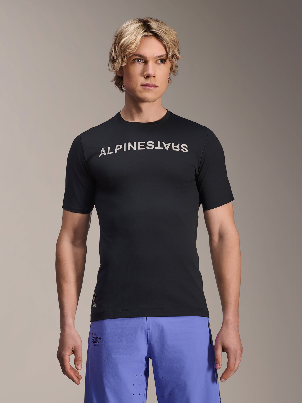 Alpinestars A-Aria Switch Trikot, Kurzarm-MTB-Trikot, Schwarz mit weißem Alpinestars-Schriftzug auf der Brust, getragen von einem männlichen Model mit lila Shorts, leichtes Performance-Gewebe für Trailriding