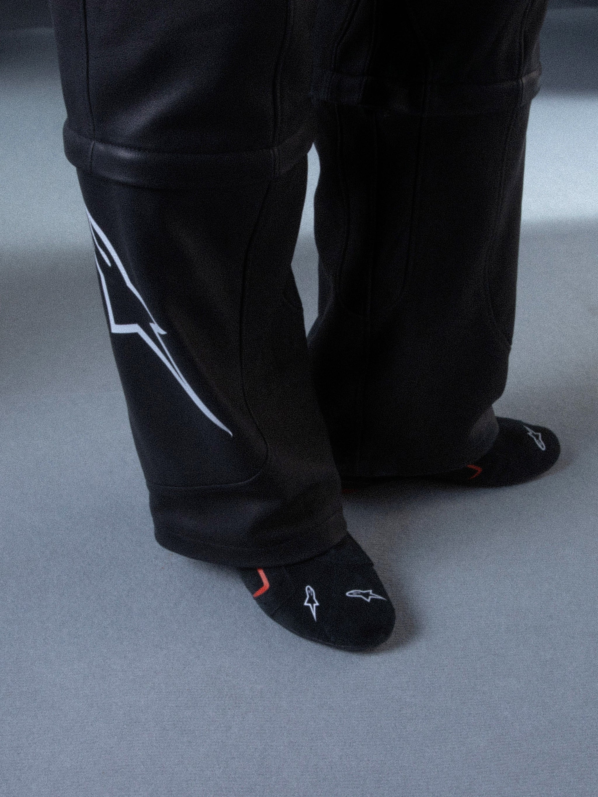 Alpinestars RSRV Starline Schuhe, Schwarze Hose mit weißem Logo an der Seite, glatte Textur mit Nähten, schwarze Socken mit weißen und roten Designs, Lifestyle-Streetwear