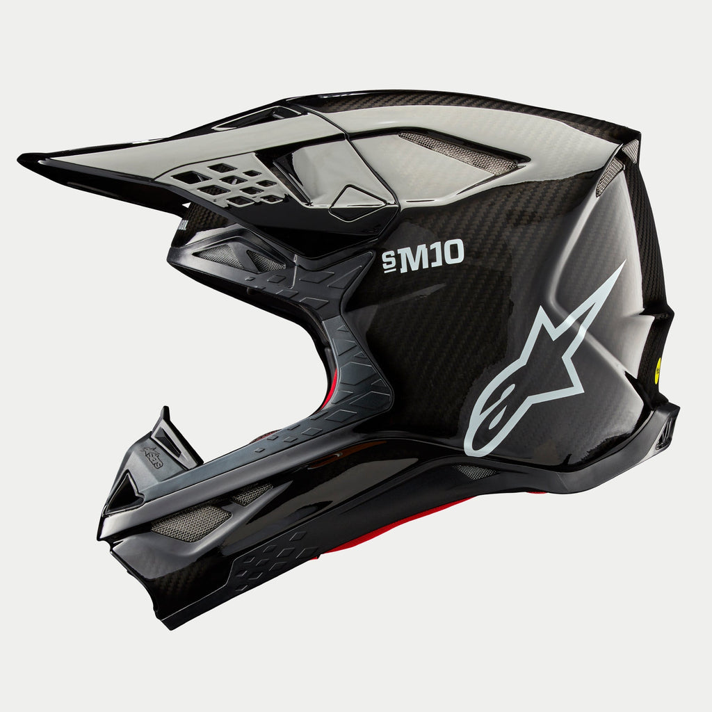 Alpinestars Supertech M10 Solid Helm, Motocross-Helm, Schwarz glänzendes Carbon, Seitenprofil mit sichtbarem Carbonfasergewebe, weißes SM10-Branding und Alpinestars-Logo, stromlinienförmiges aerodynamisches Design mit netzabgedeckten Belüftungsöffnungen