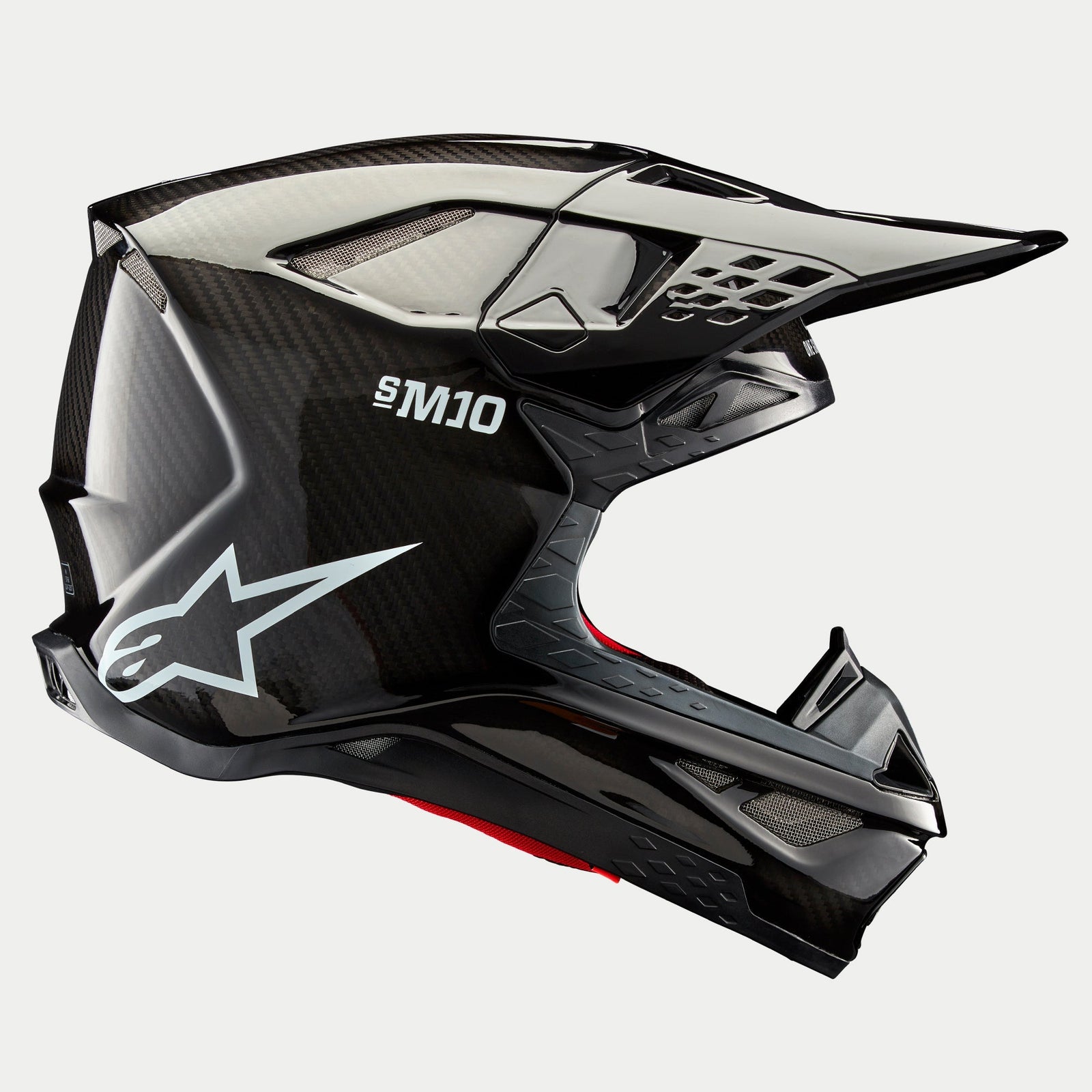Alpinestars Supertech M10 Solid Helm, Motocross-Helm, Carbon Schwarz glänzend, Seitenprofilansicht mit glänzendem Carbonfaser-Gewebe, S-M10 Branding, weißes Alpinestars Stern-Logo, aerodynamisches Design mit Helmschild und Belüftungsöffnungen