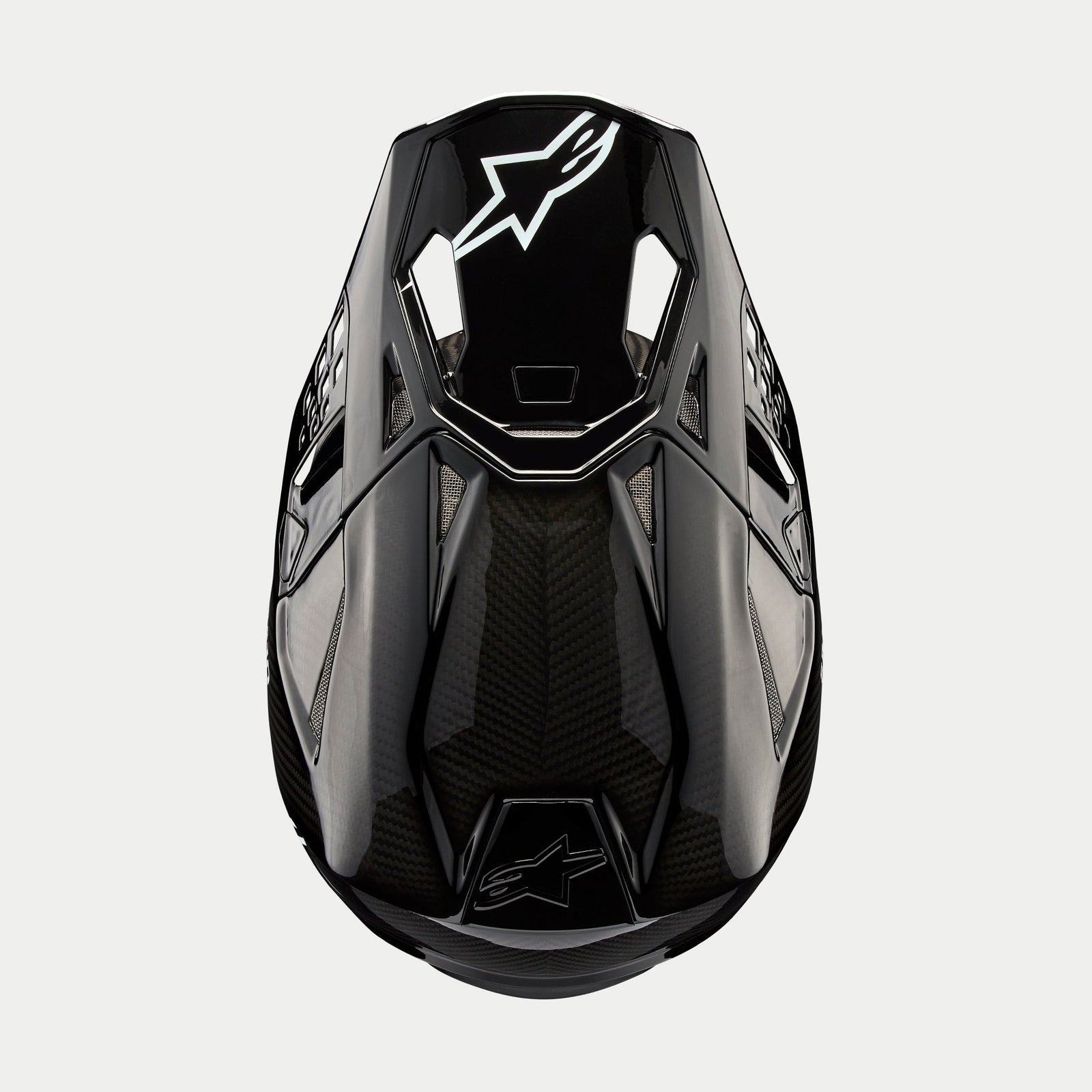 Alpinestars Supertech M10 Solid Helm, Motocross-Helm, Schwarz glänzendes Carbon, Ansicht von oben mit sichtbarem Carbonfaser-Gewebe, weißes Astars-Logo auf dem Visier, schlankes aerodynamisches Profil mit integrierten Belüftungsöffnungen