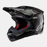 Alpinestars Supertech M10 Solid Helm, Motocross-Helm, schwarzes glänzendes Carbon mit sichtbarem Fasergewebe, mit weißem Alpinestars-Logo und SM10-Branding, rotem Innenfutter, aerodynamisches Design mit mehreren Belüftungsöffnungen
