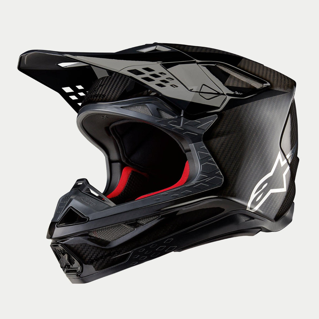 Alpinestars Supertech M10 Fame ECE 22.06 Helm, Motocross-Helm, Schwarz-Carbon in mattem und glänzendem Finish, mit sichtbarem Carbonfaser-Gewebe, weißem Astar-Logo an der Seite und roter Innenpolsterung, aerodynamisches Offroad-Design