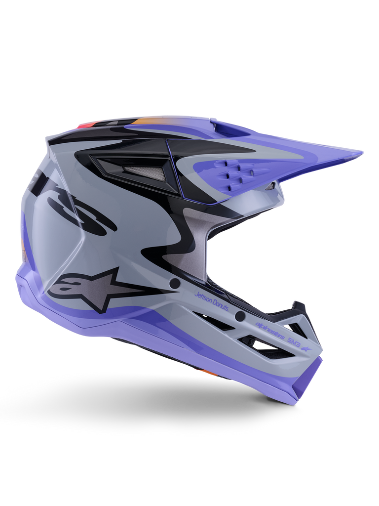 Alpinestars S-M3 Jettson Helm ECE 22.06, Motocross-Helm, Grau, Lila und Schwarz glänzend, Seitenansicht, lila Visier und Kinnschutz, schlanke aerodynamische Schale mit schwarzen Grafiken, mehrere Belüftungsöffnungen und „Jettson Donuts“-Branding auf der Seite.