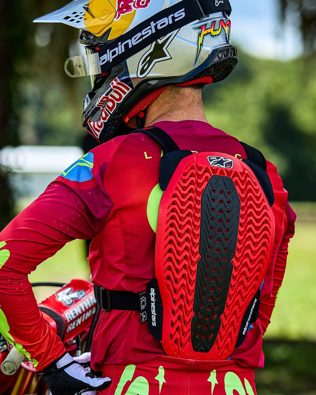 Motocross-Fahrer von hinten gesehen mit dem Alpinestars A-5 Plasma Brustprotektor, bestehend aus einem rot-schwarzen Rückenprotektor mit belüfteter Wabenstruktur, getragen über einem roten Langarmtrikot und einem Red Bull-Helm.