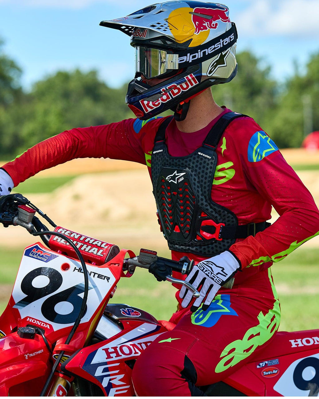 Motocross-Fahrer mit Alpinestars A-5 Plasma Brustprotektor in Schwarz und Rot, kombiniert mit einem Rennsport-Trikot und einer Hose in Rot und Limettengrün, sitzend auf einem roten Honda-Motorrad, Hochleistungs-Offroad-Schutzausrüstung