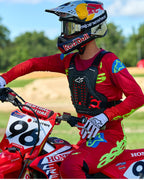 Motocross-Fahrer mit Alpinestars A-5 Plasma Brustprotektor in Schwarz und Rot, kombiniert mit einem Rennsport-Trikot und einer Hose in Rot und Limettengrün, sitzend auf einem roten Honda-Motorrad, Hochleistungs-Offroad-Schutzausrüstung