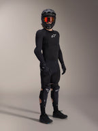 Alpinestars A-Impact Plasma Pro Knie-Schienbein-Protektoren, Schwarz und Weiß, getragen von einem Fahrer mit kompletter Mountainbike-Schutzausrüstung, inklusive schwarzem langärmeligem Protektoren-Oberteil, schwarzen Handschuhen und Fullface-Helm mit orangefarbener Goggle.