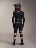 Alpinestars A-Impact Plasma Pro Knie-Schienbeinschützer, Schwarz, Rückansicht eines Fahrers in kompletter Mountainbike-Schutzausrüstung inklusive Fullface-Helm und Body Armor, mit Dreifach-Riemen-Verschlusssystem und belüfteten Mesh-Einsätzen für sicheren Sitz und Luftzirkulation