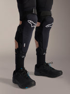 Alpinestars A-Impact Plasma Pro Knie-Schienbein-Schützer, Schwarz und Weiß, mit weißem Alpinestars-Logo und Dreifach-Riemen-Verschlusssystem, getragen mit schwarzen Socken und schwarzen Sportschuhen, strapazierfähiger Schutz für den Offroad-Radsport