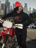 Alpinestars Pulse Hoodie, Schwarz, Kapuzenpullover aus Fleece mit rot-grauem Astars Combo Logo, getragen von einem Mann mit orangefarbener Beanie neben einem roten Honda-Motorrad in einer städtischen Umgebung, lässige Motorsport-Streetwear