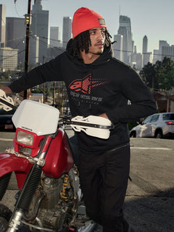 Alpinestars Pulse Hoodie, Schwarz, Kapuzenpullover aus Fleece mit rot-grauem Astars Combo Logo, getragen von einem Mann mit orangefarbener Beanie neben einem roten Honda-Motorrad in einer städtischen Umgebung, lässige Motorsport-Streetwear